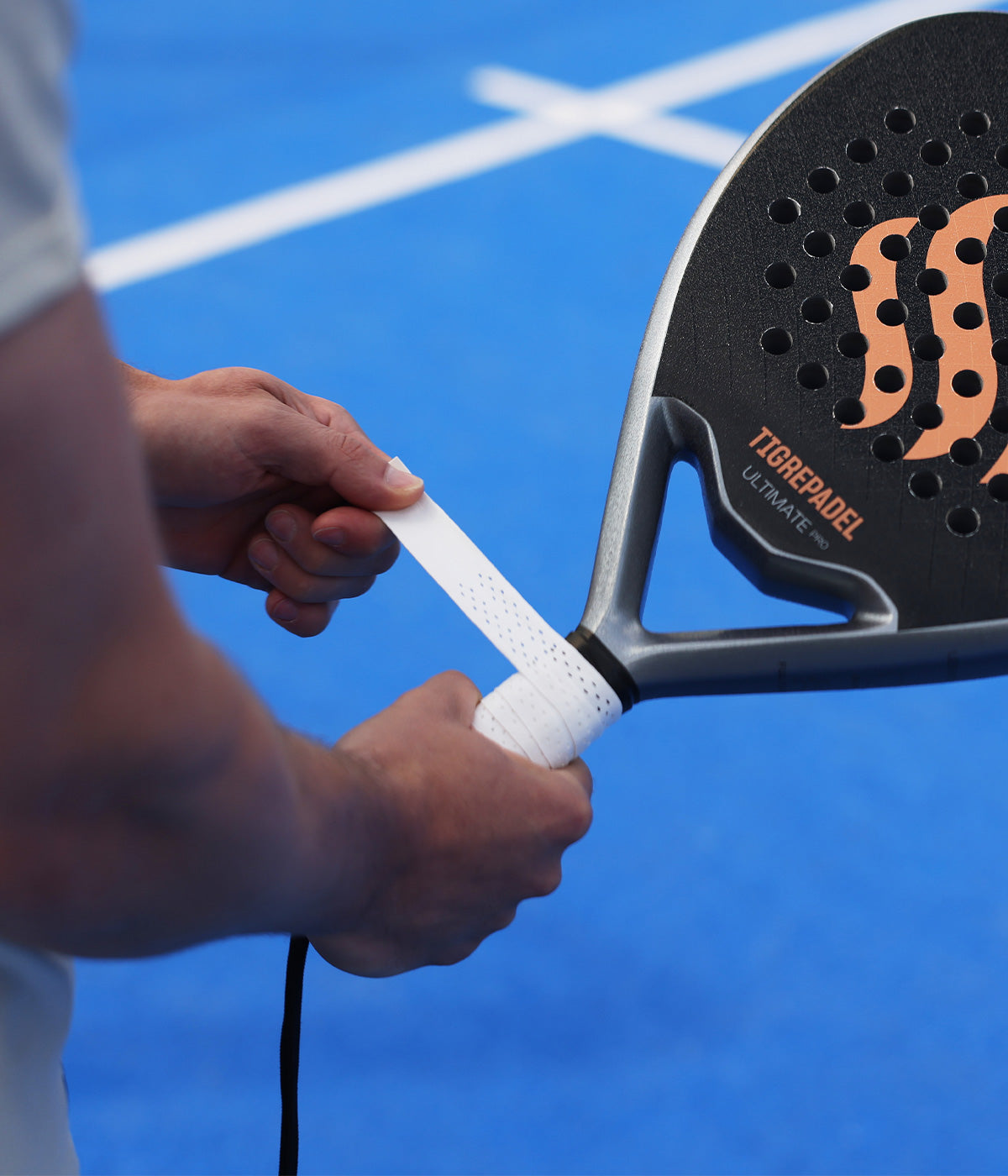 Speler brengt een witte padel overgrip van TigrePadel aan op zijn padelracket op ede padelbaan.